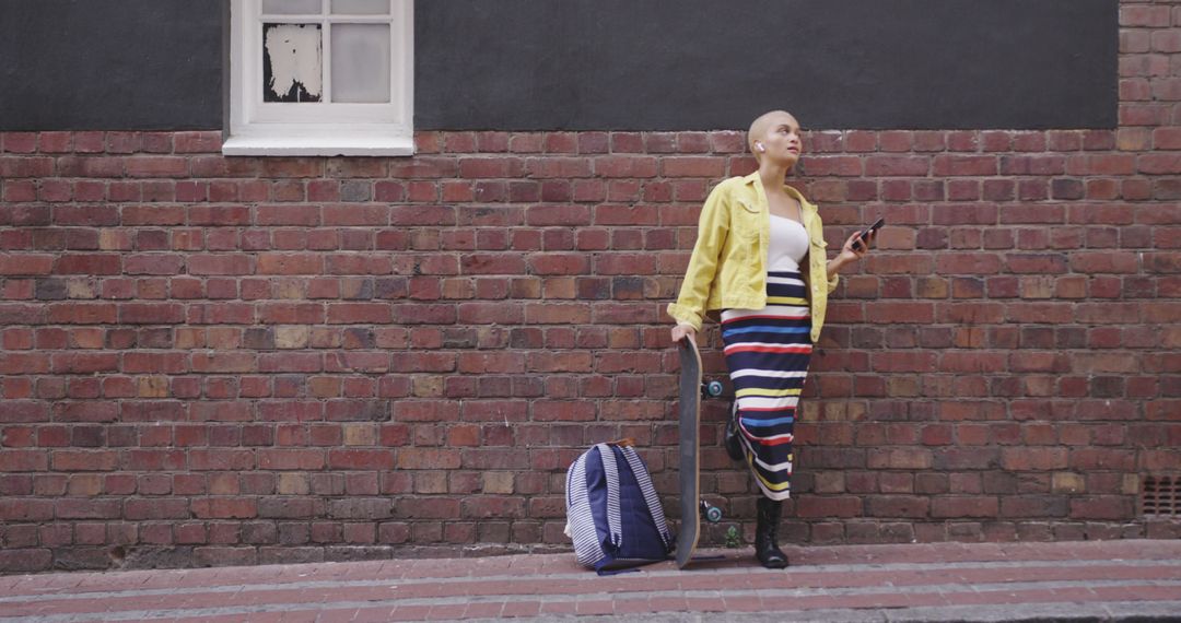 Biracial woman leaning on brick wall, holding skateboard and smartphone, copy space - Free Images, Stock Photos and Pictures on Pikwizard.com