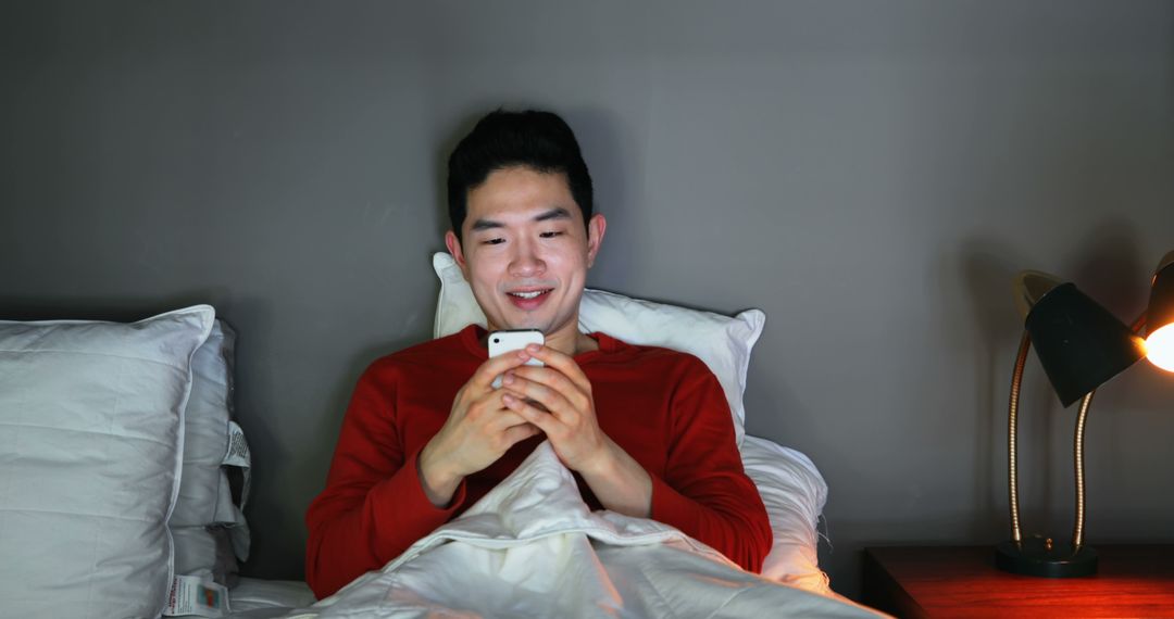 Young Man Smiling While Using Smartphone in Bed at Night - Free Images, Stock Photos and Pictures on Pikwizard.com