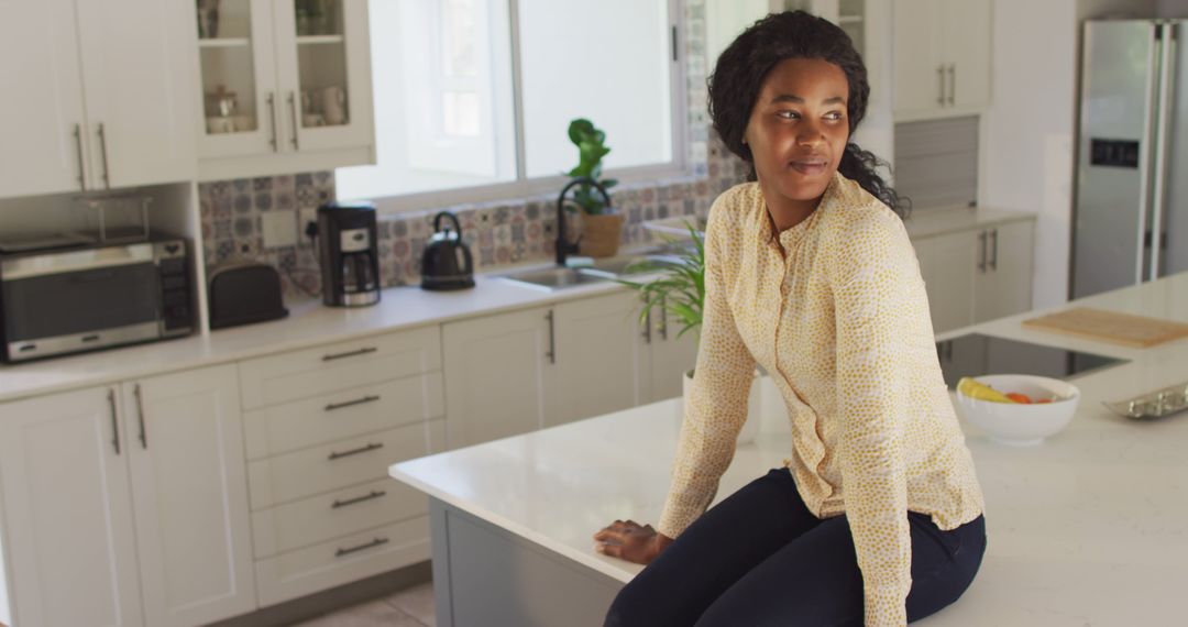 Image of happy african american woman sitting on countertop in kitchen - Free Images, Stock Photos and Pictures on Pikwizard.com