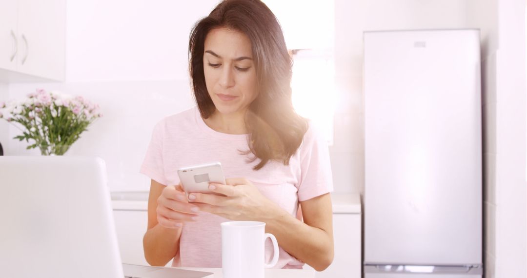 Woman Using Smartphone at Kitchen Table in Bright Morning Light - Free Images, Stock Photos and Pictures on Pikwizard.com