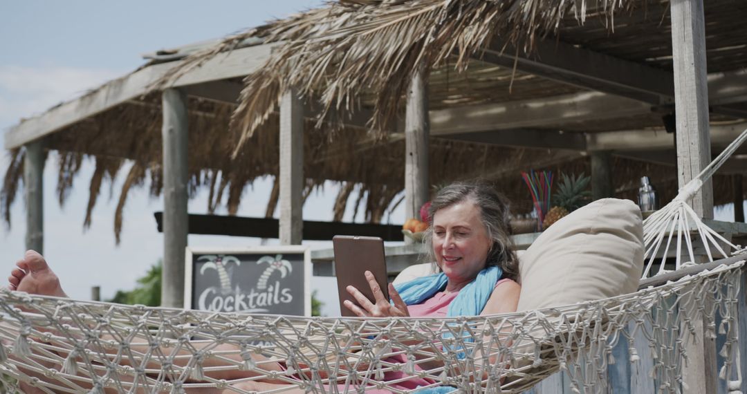 Mature Woman Relaxing in Hammock with Tablet at Tropical Beach Bar - Free Images, Stock Photos and Pictures on Pikwizard.com