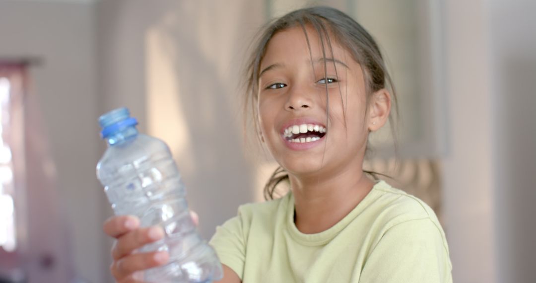 Smiling Biracial Girl Holding Plastic Bottle for Recycling at Home