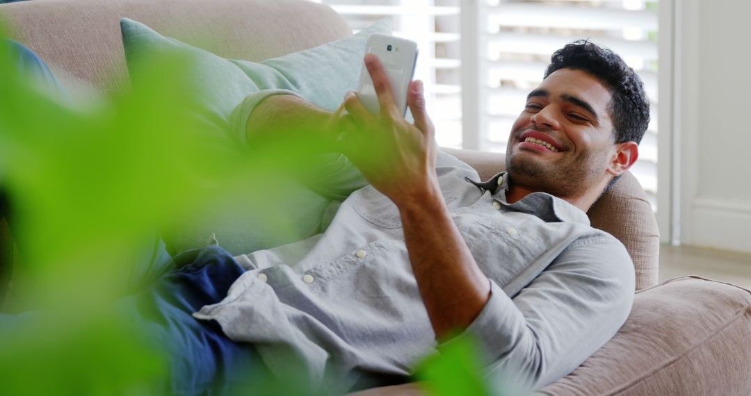 Young Man Relaxing on Couch and Looking at Smartphone - Free Images, Stock Photos and Pictures on Pikwizard.com