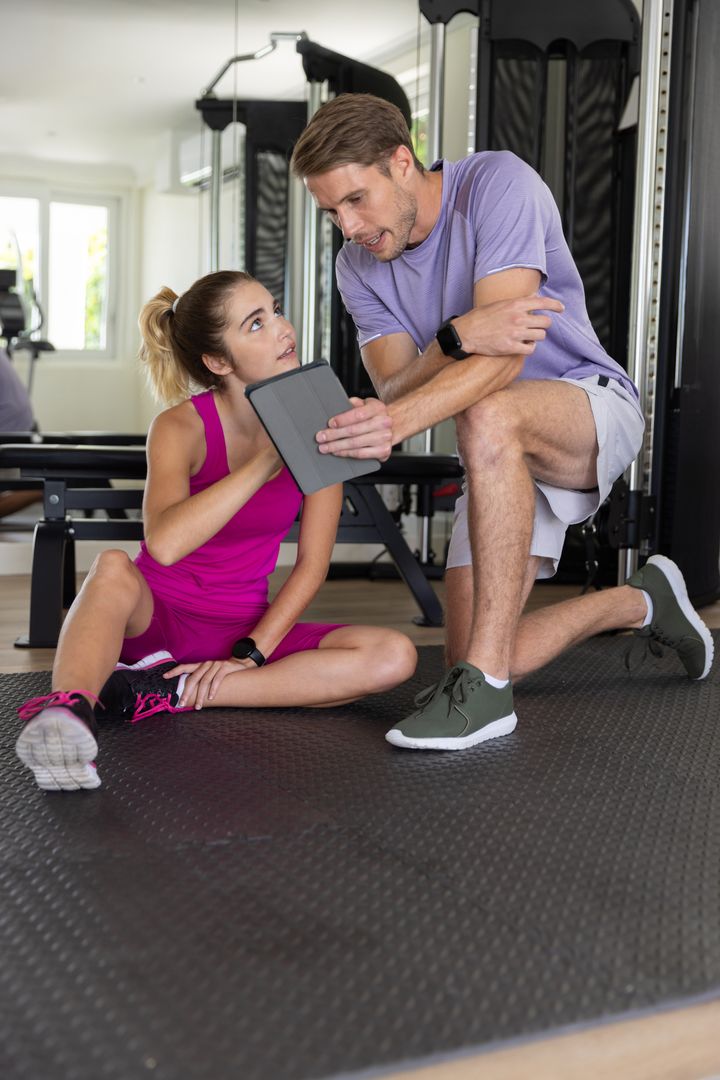 Personal Trainer Guiding Client with Tablet in Gym Setting