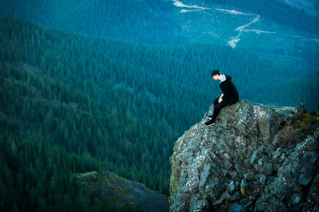 Man Sitting on Cliff Edge Overlooking Forest Valley - Free Images, Stock Photos and Pictures on Pikwizard.com