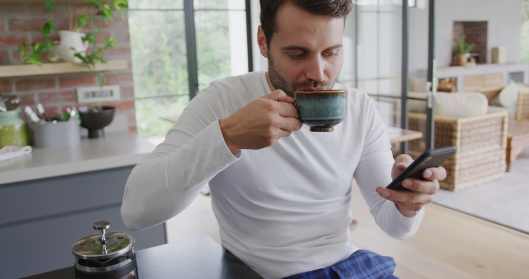 Young man in modern kitchen drinking coffee and checking smartphone - Free Images, Stock Photos and Pictures on Pikwizard.com