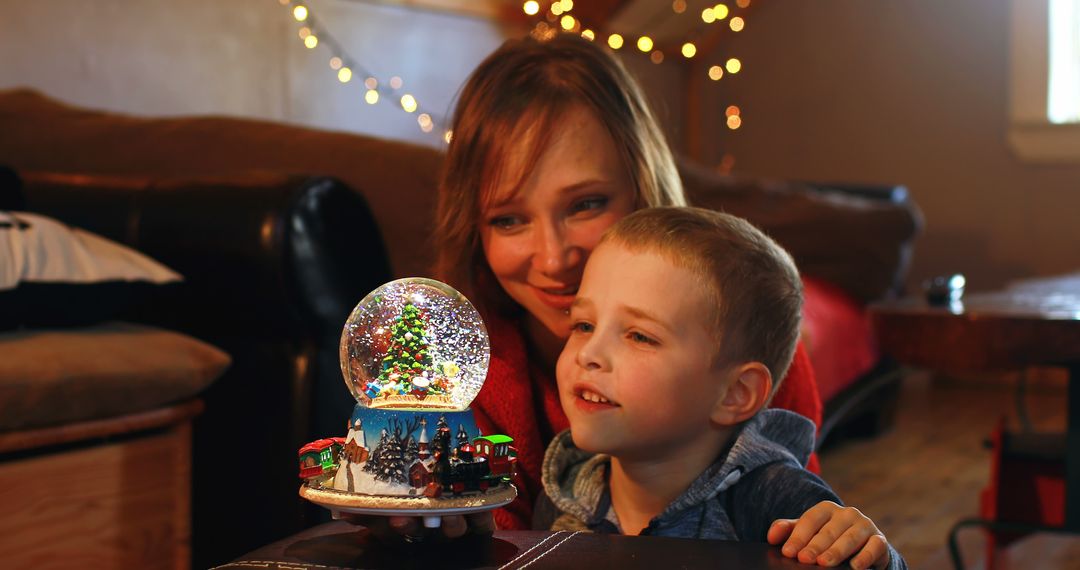 Mother and Son Gazing at Christmas Snow Globe with Lights in Background - Free Images, Stock Photos and Pictures on Pikwizard.com