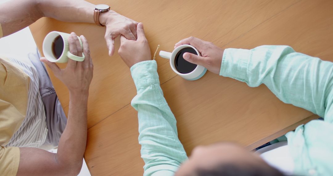 Top view of two friends holding hands and drinking coffee together - Free Images, Stock Photos and Pictures on Pikwizard.com