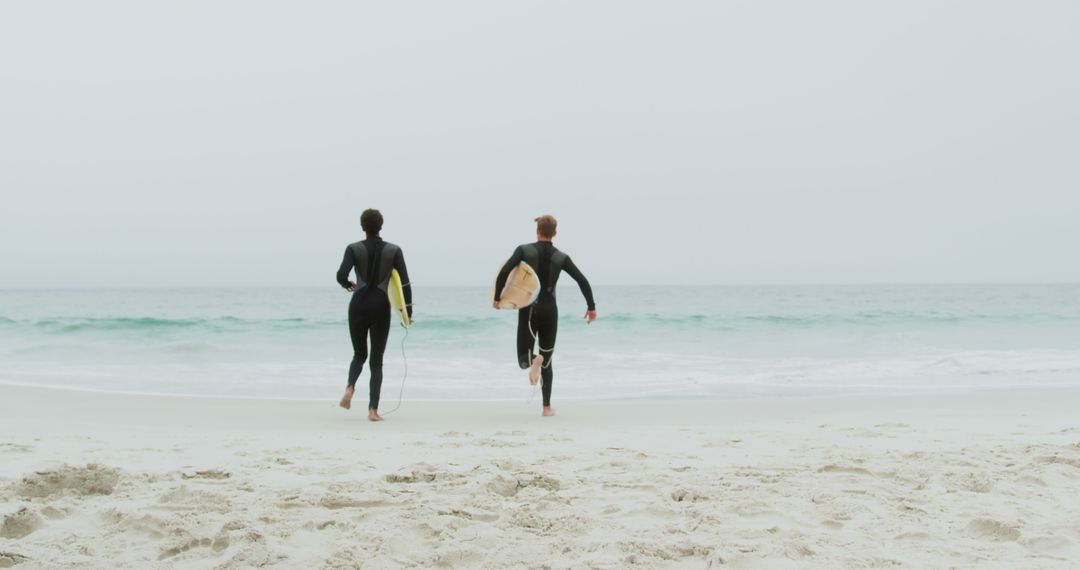 Adventurous Surfers Running on Sandy Beach with Surfboards