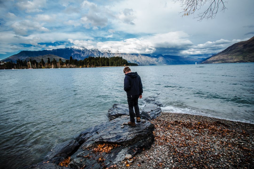 Man Standing on Rocky Shore Looking at Scenic Lake and Mountains - Free Images, Stock Photos and Pictures on Pikwizard.com