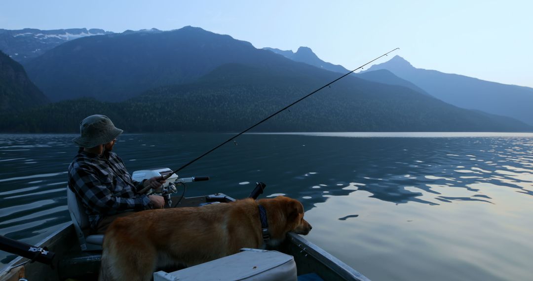 A man and his dog experience peaceful fishing amidst mountains, embodying serene companionship. - Free Images, Stock Photos and Pictures on Pikwizard.com