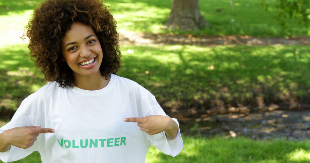 Cheerful Volunteer Pointing at T-Shirt Outdoors on Sunny Day - Free Images, Stock Photos and Pictures on Pikwizard.com