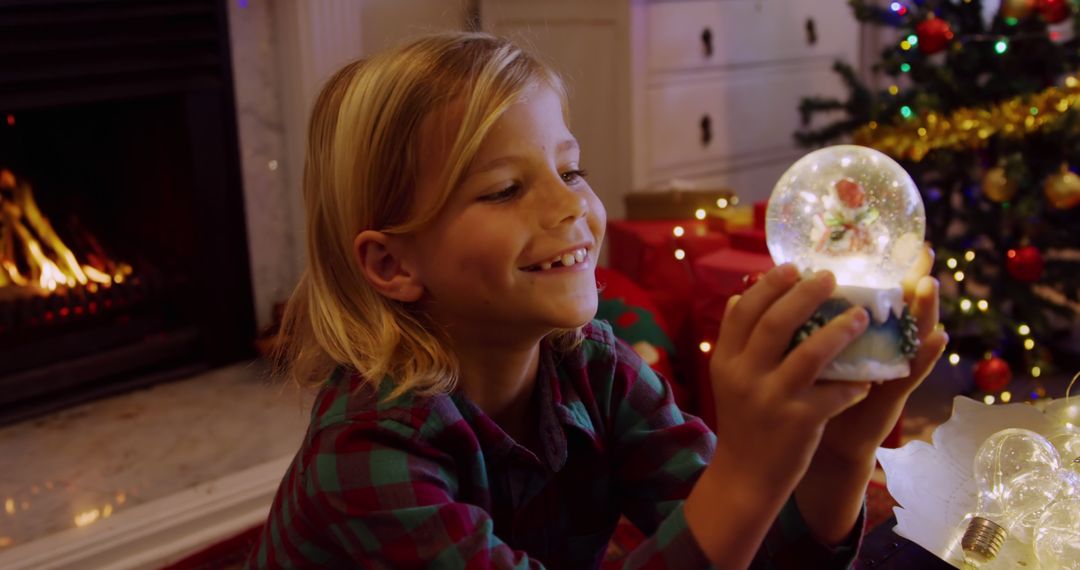 Happy Child Admiring Snow Globe Near Christmas Tree - Free Images, Stock Photos and Pictures on Pikwizard.com