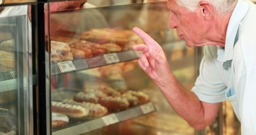 Senior Man Pointing at Bakery Display Case with Assorted Pastries - Free Images, Stock Photos and Pictures on Pikwizard.com