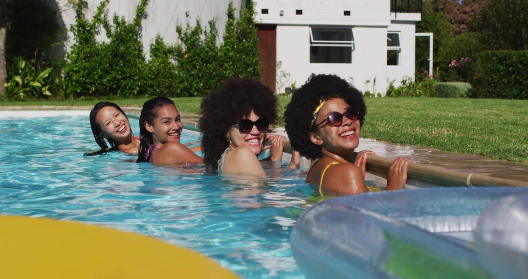 Four Friends Laughing and Relaxing in Sunlit Backyard Pool Wearing Summer Swimwear