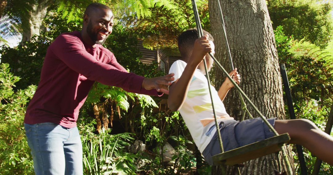 African american dad pushing his son on a swing in the garden on a bright sunny day - Free Images, Stock Photos and Pictures on Pikwizard.com