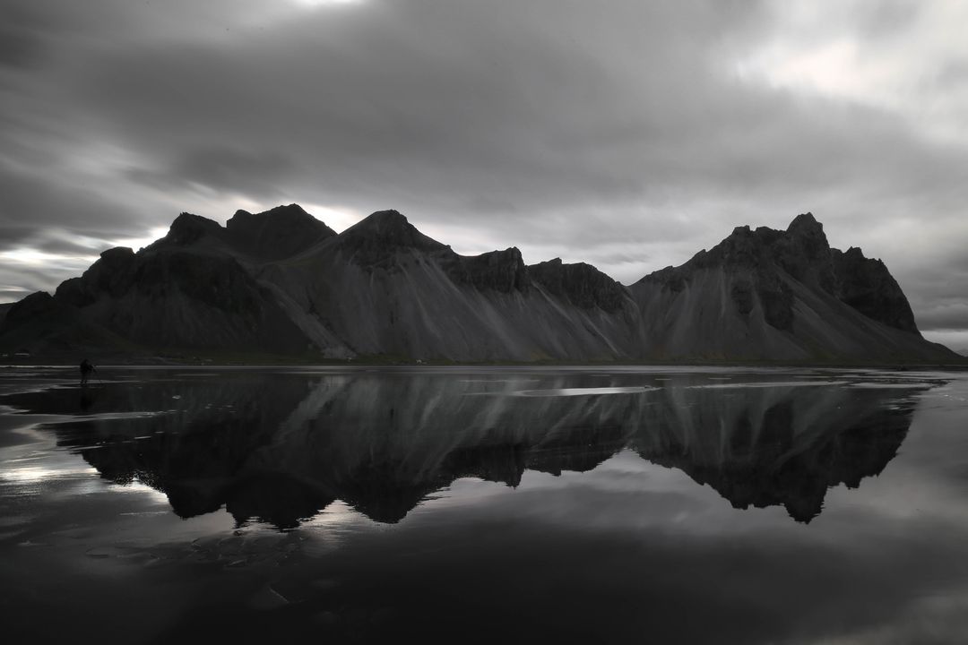 Dramatic black and white coastal mountain range reflecting on still tidal mirror under moody sky