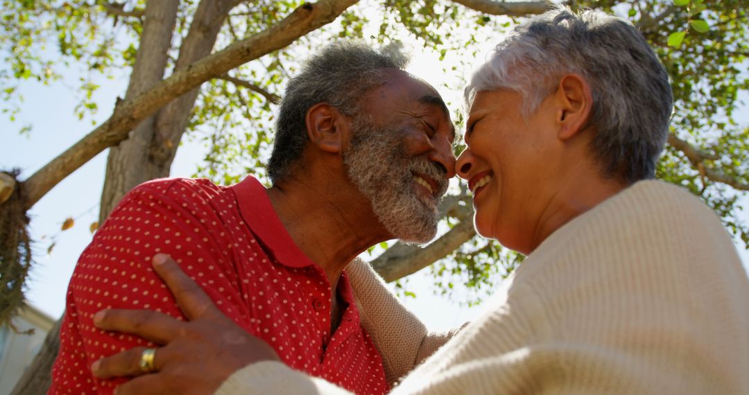 Happy Senior Couple Embracing Under Tree with Smiles
