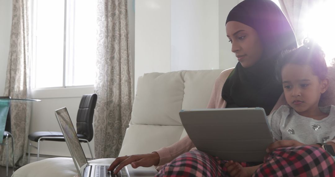 Busy Parent Wearing Hijab Multitasking with Child in Living Room