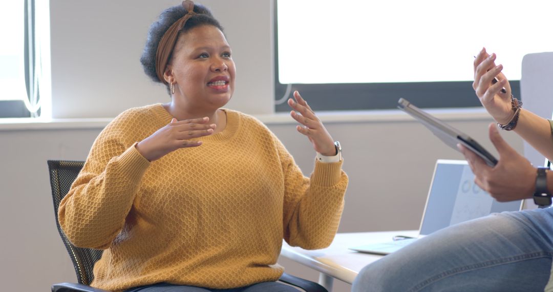 Workplace collaboration showing woman in mustard sweater leading discussion with colleague
