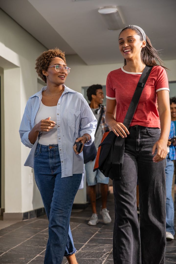 Diverse teenage friends walking and talking in school hallway carrying backpacks, phones