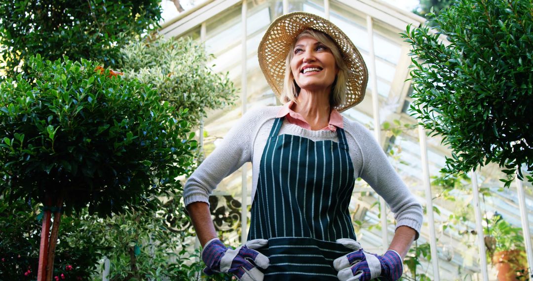 Smiling Woman in Gardening Clothes Standing in Greenhouse - Free Images, Stock Photos and Pictures on Pikwizard.com