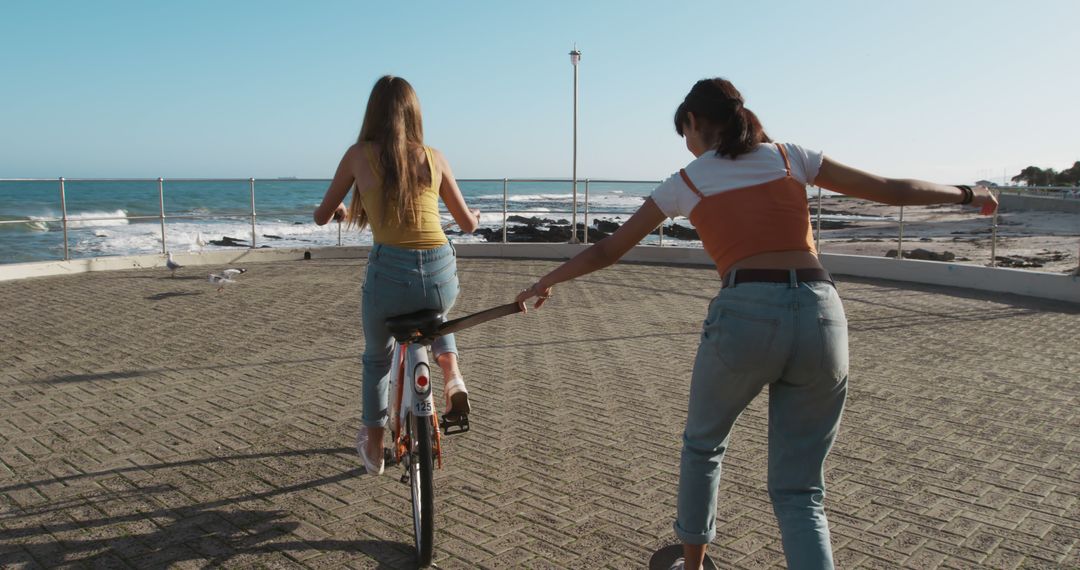 Two Young Women Riding Bike at Seaside Promenade on Sunny Day - Free Images, Stock Photos and Pictures on Pikwizard.com