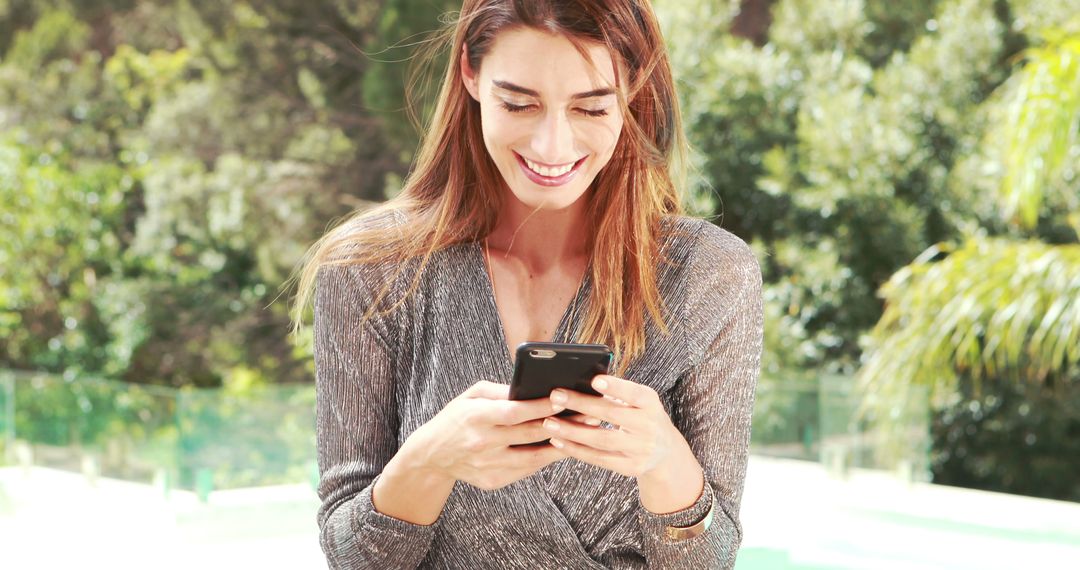 Smiling Woman Texting on Smartphone in Sunlit Outdoor Environment - Free Images, Stock Photos and Pictures on Pikwizard.com