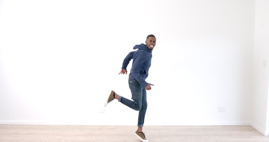 Joyful Man in Blue Hoodie Jumping Indoors Amidst White Space