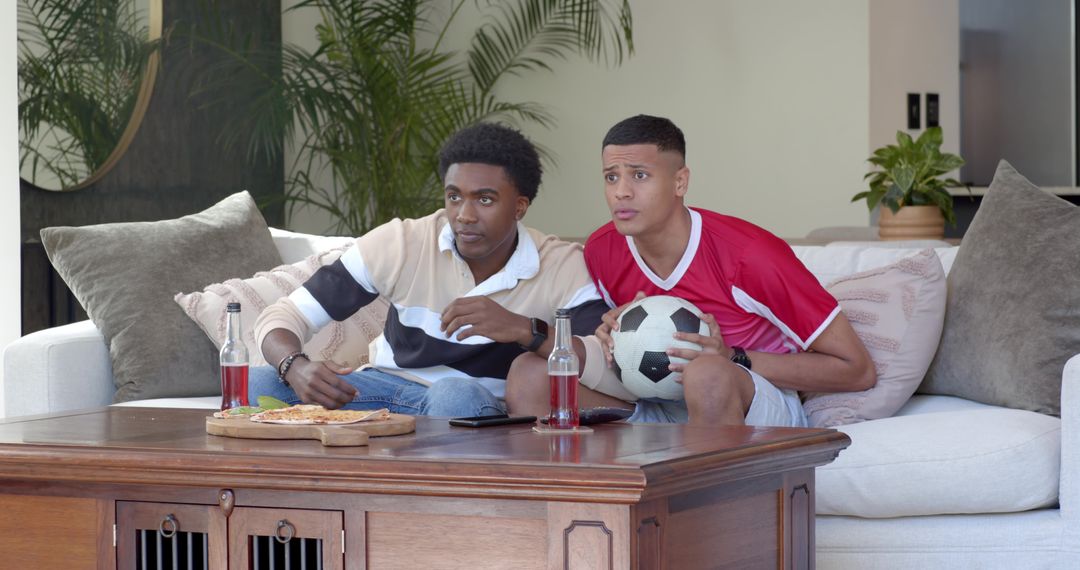 Friends Watching Football Sharing Pizza On Sofa Enthusiastically