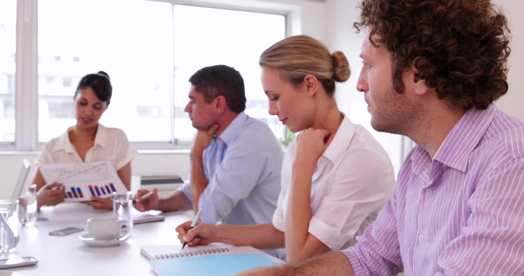 Female Presenter Leading Business Team Reviewing Charts and Taking Notes in Meeting Room