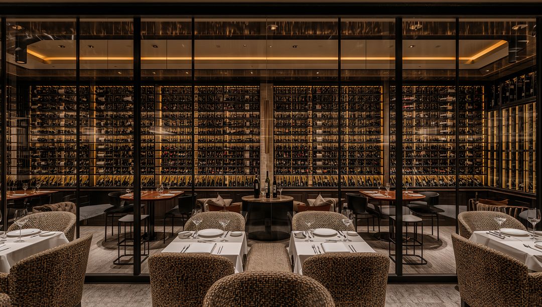 Luxury wine wall featuring backlit racks and intimate linen dining with woven armchairs