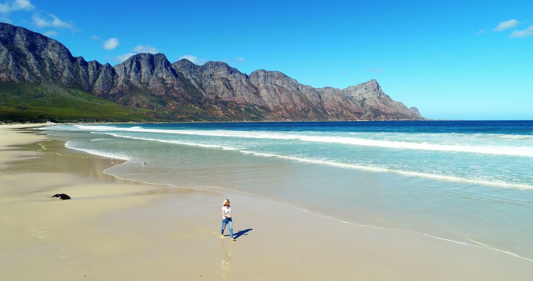 Solitary Walk on Scenic Beach with Majestic Mountain Backdrop