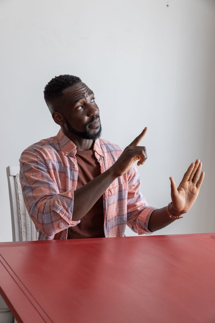 Man Wearing Pink Plaid Shirt Gesturing at Red Table