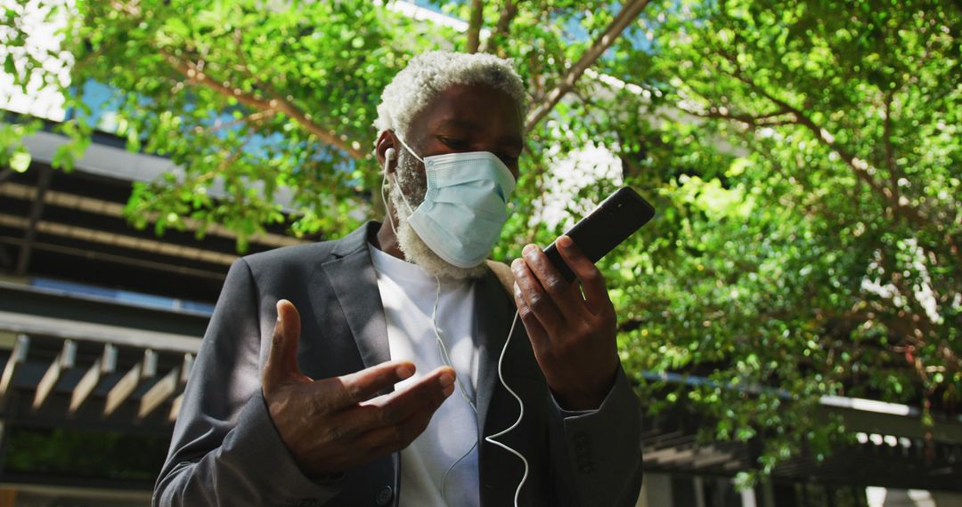 Senior Man with Mask Using Smartphone and Earphones Outdoors - Free Images, Stock Photos and Pictures on Pikwizard.com