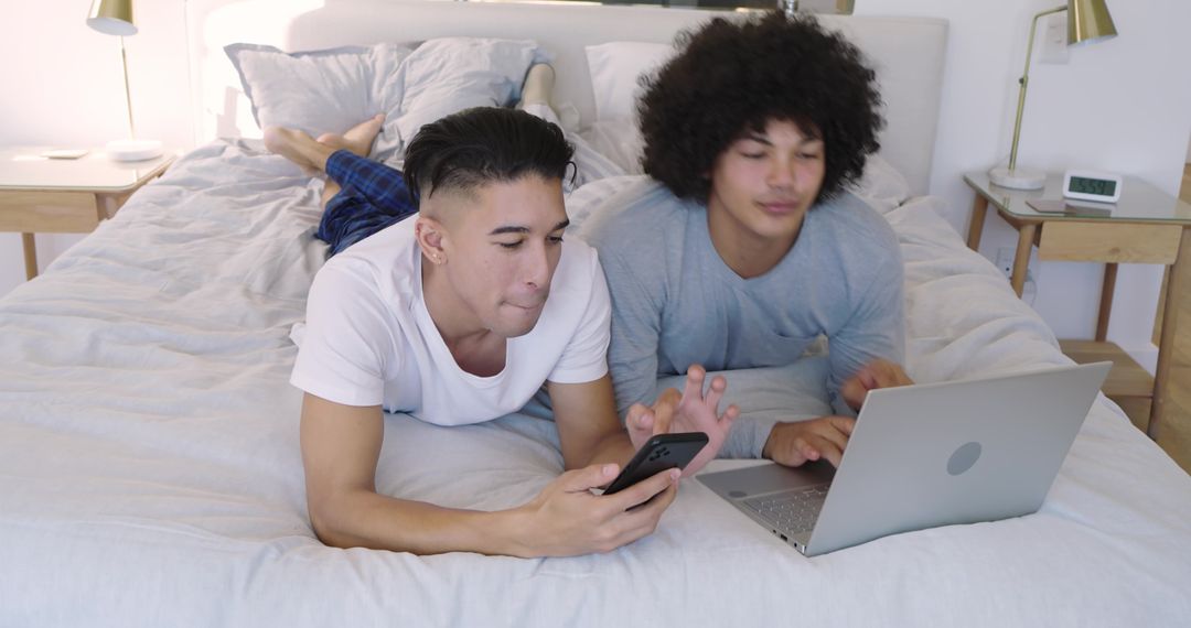 Roommates Relaxing with Technology on a Cozy Bed