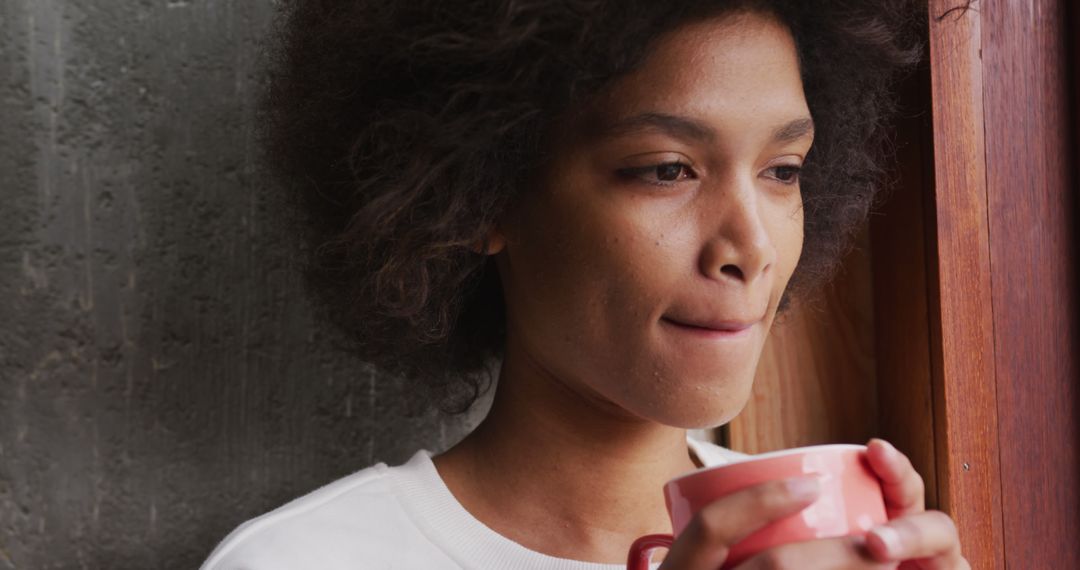 Young Woman Drinking Coffee by Window with Thoughtful Expression - Free Images, Stock Photos and Pictures on Pikwizard.com