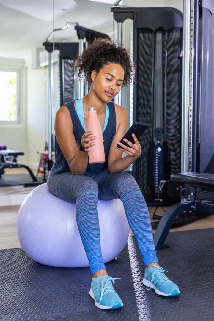 Woman Exercising in Gym Relaxing on Stability Ball Checking Smartphone