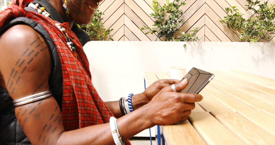 Smiling African Man in Traditional Attire Using Tablet Computer at Outdoor Cafe - Free Images, Stock Photos and Pictures on Pikwizard.com