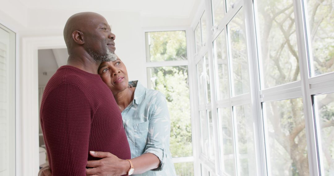 Elderly Couple Embracing and Looking Out Bright Window - Free Images, Stock Photos and Pictures on Pikwizard.com