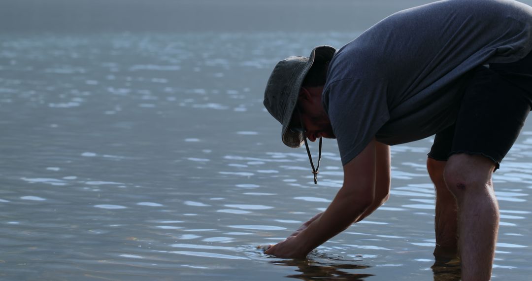 Man Wearing Hat Gathering Water in Peaceful Lake Setting - Free Images, Stock Photos and Pictures on Pikwizard.com