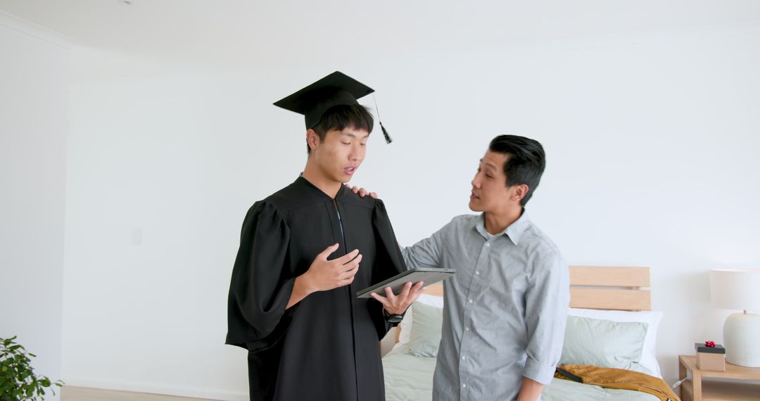 Father Congratulating Son in Graduation Gown Receiving Gift