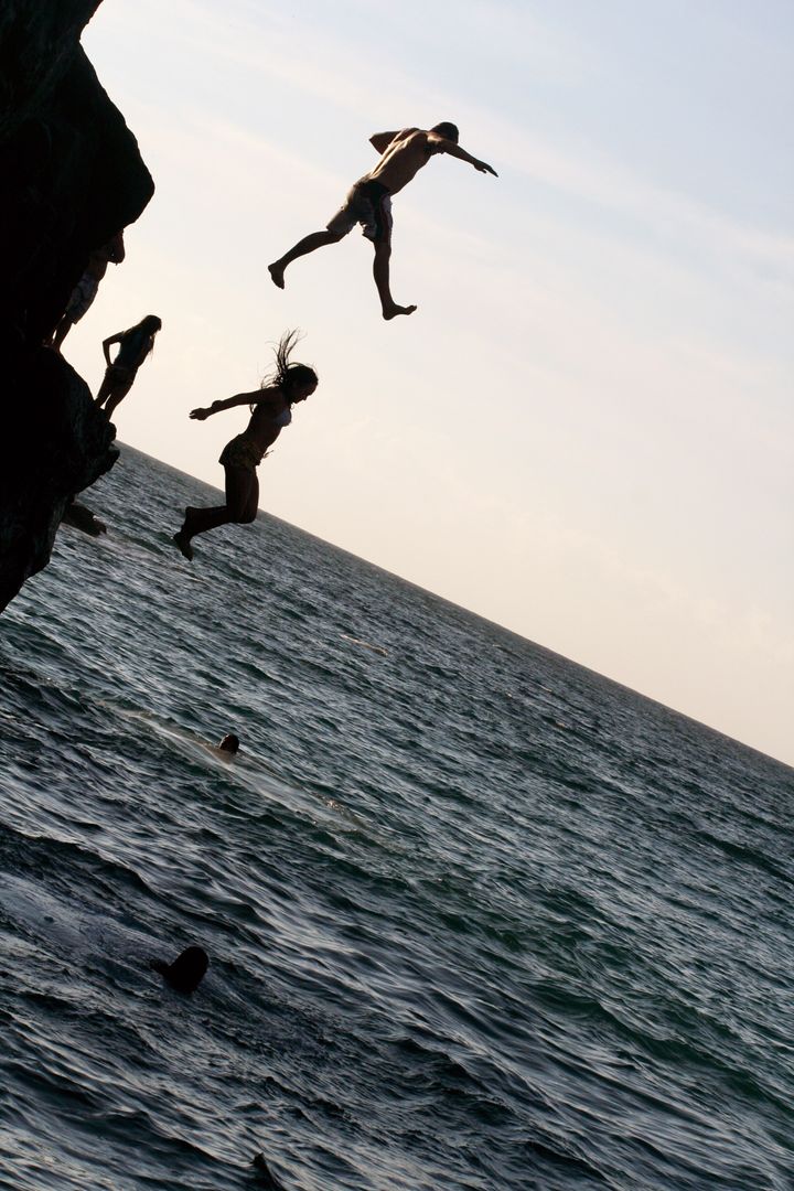 Joyful Moment of People Cliff Jumping into Sea