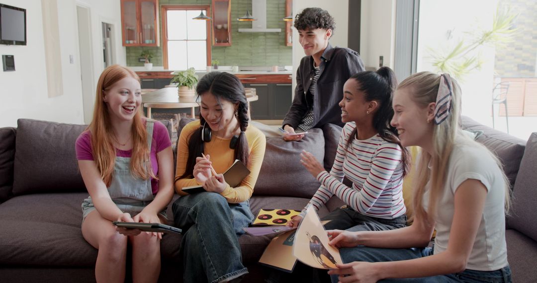 Diverse friends laughing and sharing tablet, notebook and vinyl records on sofa