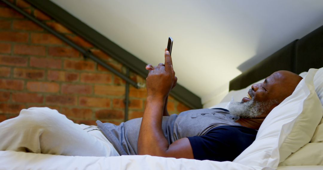 Older Man Lying in Bed Laughing While Using Phone - Free Images, Stock Photos and Pictures on Pikwizard.com