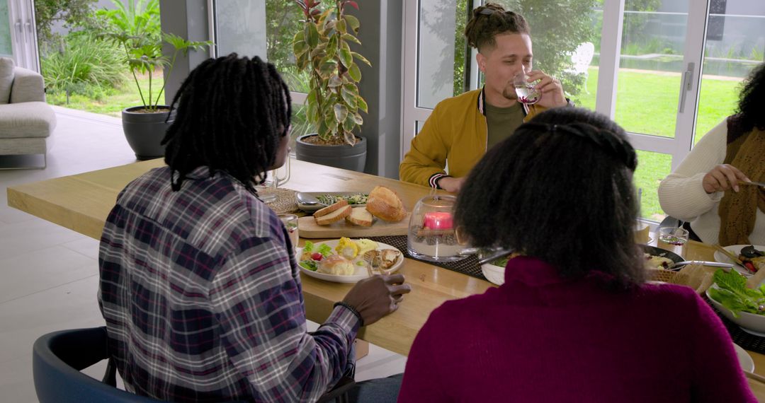 Friends Sharing Casual Brunch Around Sunlit Modern Dining Table with Bread Salad Wine