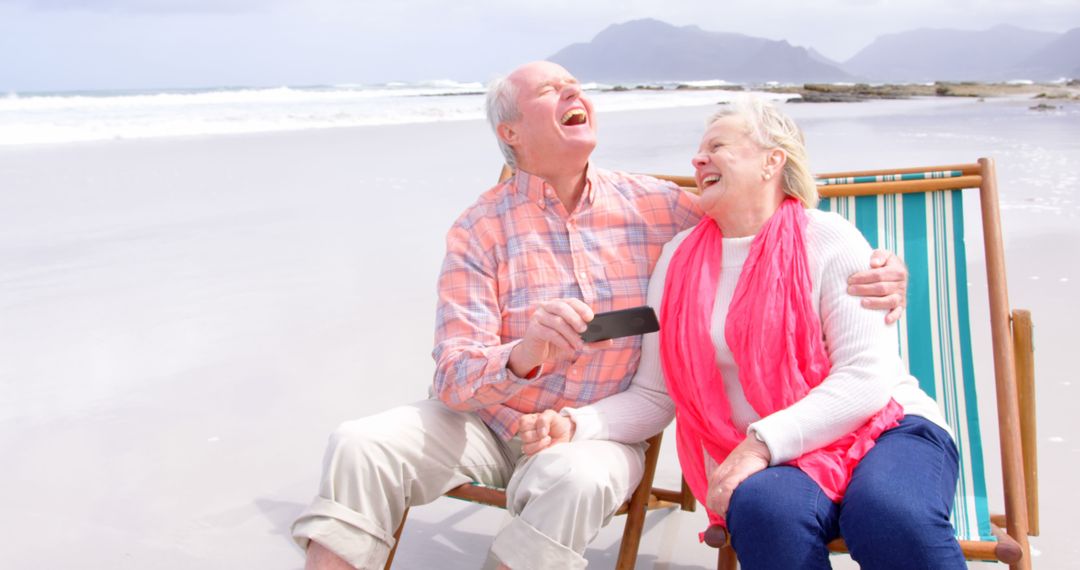 Happy Senior Couple Laughing on Beach Chairs by the Ocean - Free Images, Stock Photos and Pictures on Pikwizard.com