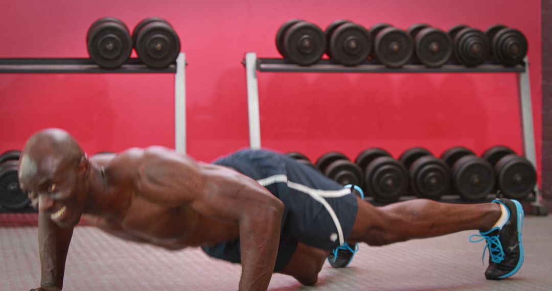 Muscular man performing push-ups in gym with weights in background - Free Images, Stock Photos and Pictures on Pikwizard.com