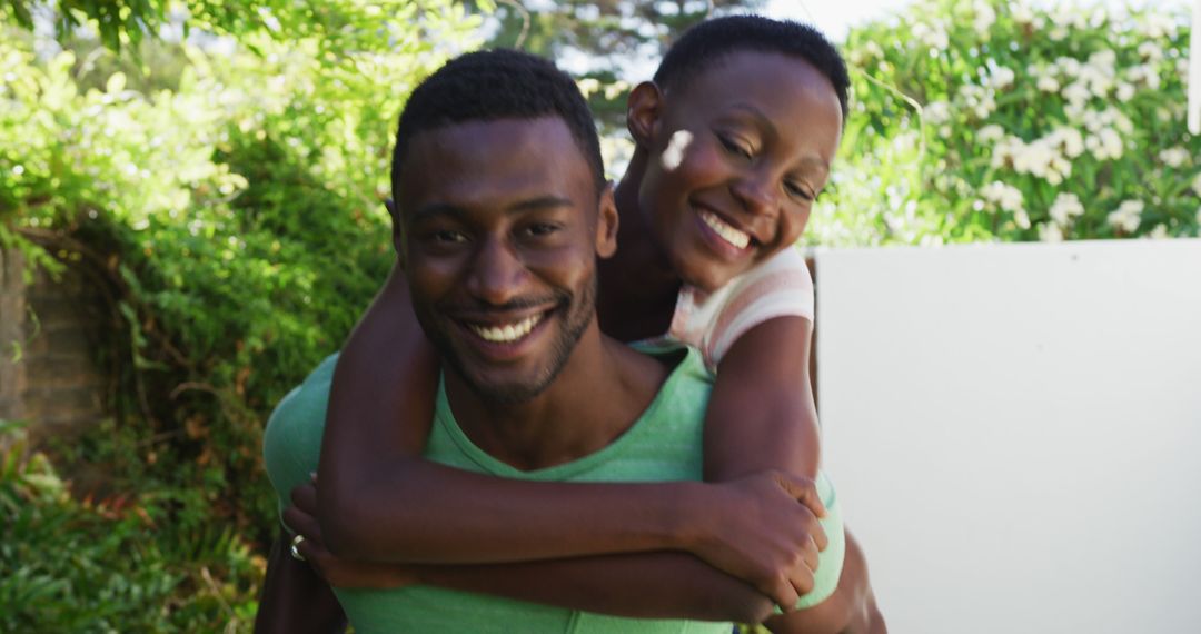 Happy african american couple having fun piggybacking in sunny garden and smiling - Free Images, Stock Photos and Pictures on Pikwizard.com