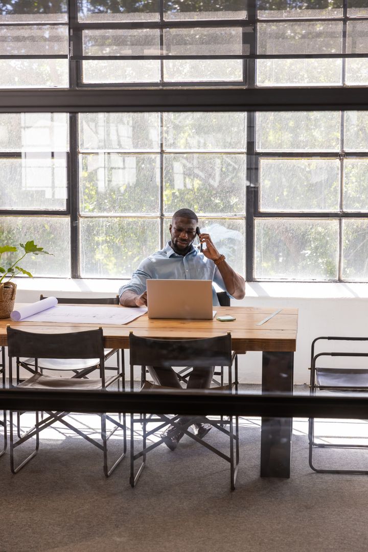 Businessman Discussing While Checking Content on Laptop and Blueprint Desk